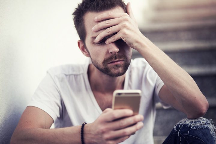 stressed man with hand covering face looking down at cell phone - pandemic - stress