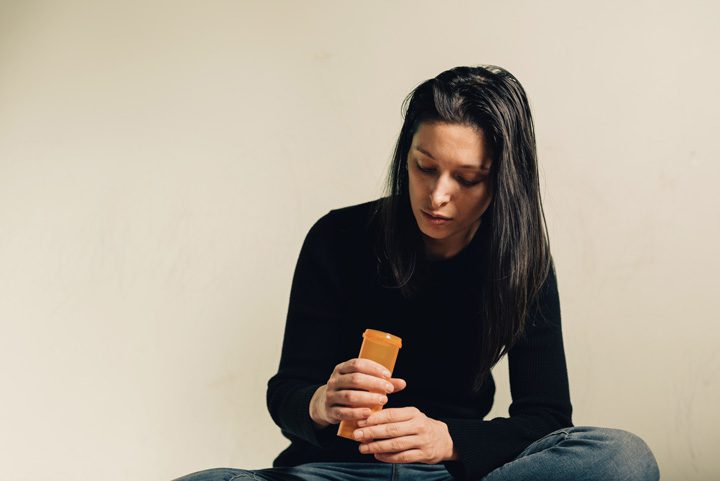 woman looking into empty prescription bottle - signs of prescription drug abuse