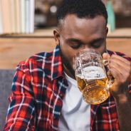 Drug and Alcohol Relapse, addiction relapse, young African American man in plaid shirt drinking a beer from a glass mug - alcohol detox