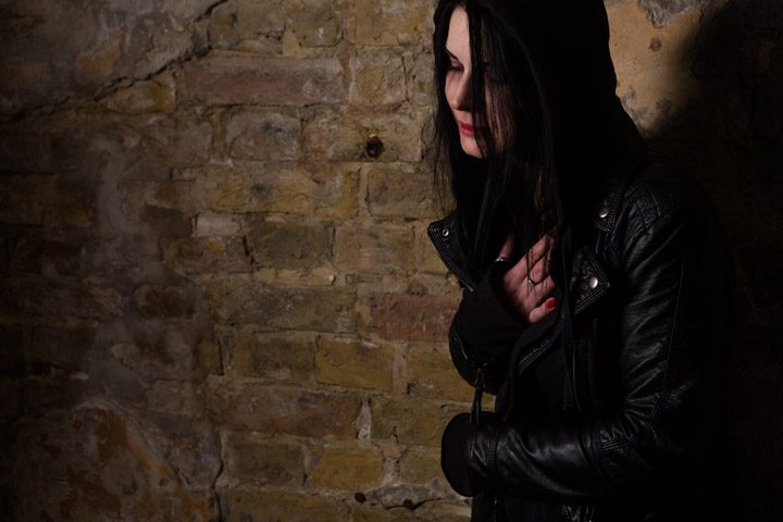 dark haired young woman in black leather jacket looking sick or upset in alley - meth