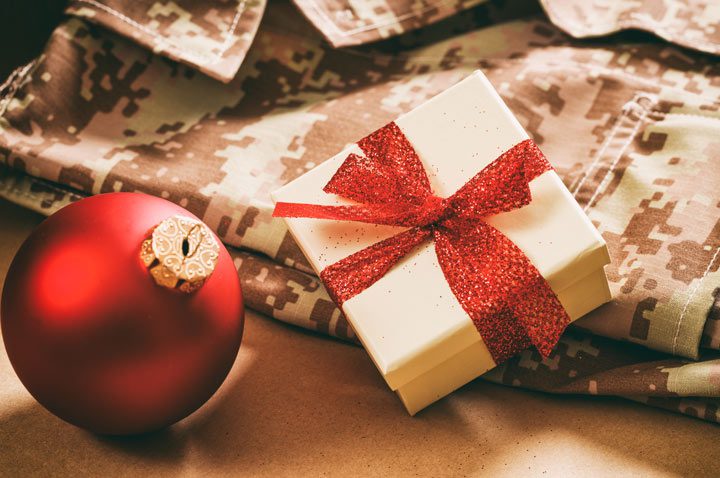 closeup of digital camouflage fatigues on floor with a small Christmas present and red tree ornament lying on them - veterans and the holidays