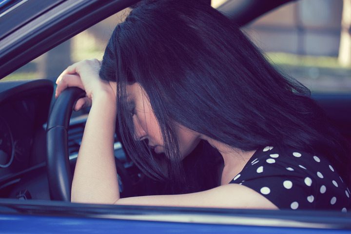 closely cropped shot of woman through her open car window, leaning against the steering wheel - drunk driving