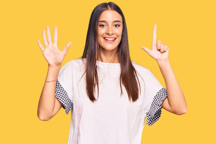 pretty young woman making the hand sign for the number seven on a bright yellow background - addiction recovery