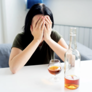 A visibly upset woman sitting in front of a glass of alcohol.