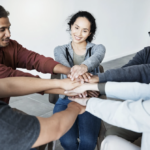 A circle of people with their hands in the middle.