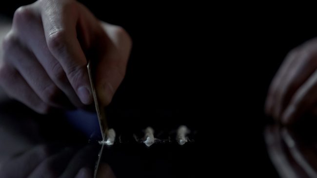 person cutting up lines of cocaine on glass table - cocaine addiction