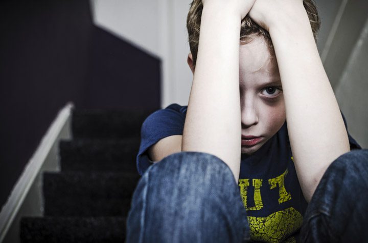 sad little boy sitting on steps with arms covering most of his sad face - past trauma