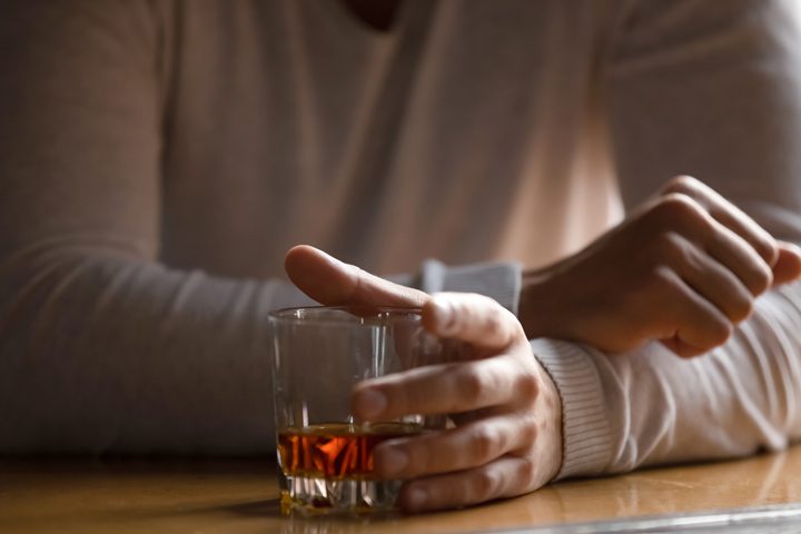 closeup of man sitting with tumbler of liquor - alcoholism