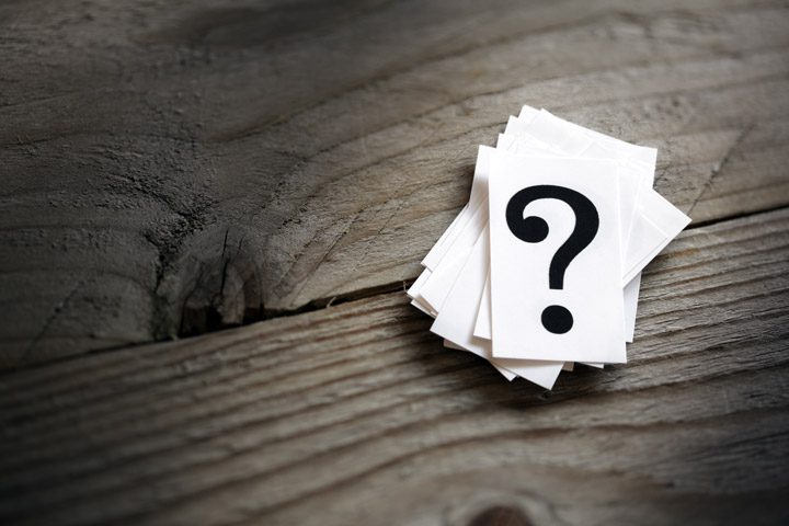 pile of black question marks on small squares of white paper sitting on a wooden table - back to work