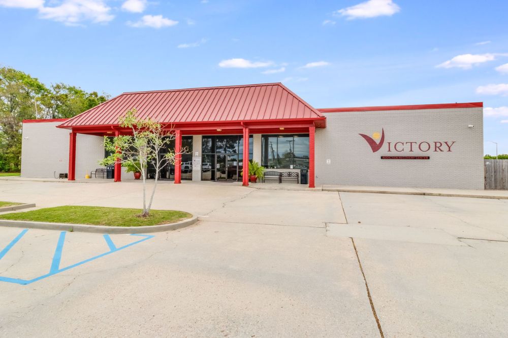 Exterior view of Victory Addiction Recovery Center in Lafayette, Louisiana, featuring a red roof, light gray brick walls, and clear signage near the main entrance.