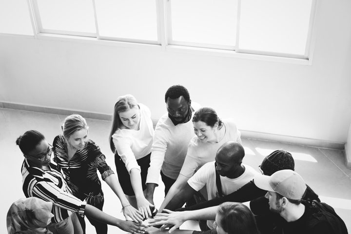 black and white image of people putting hands in circle - program