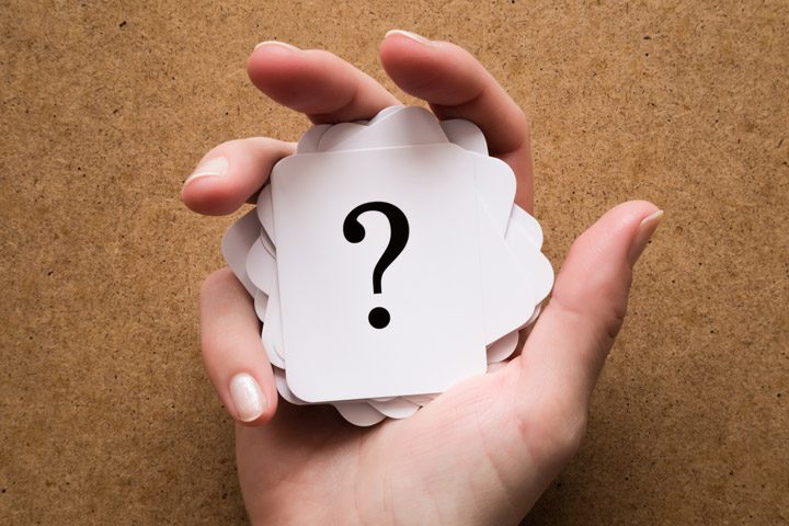 hand holding a stack of white cards with black question marks on them - drug and alcohol addiction