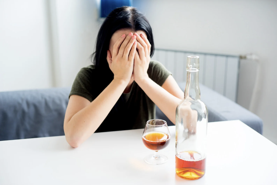 A visibly upset woman sitting in front of a glass of alcohol.