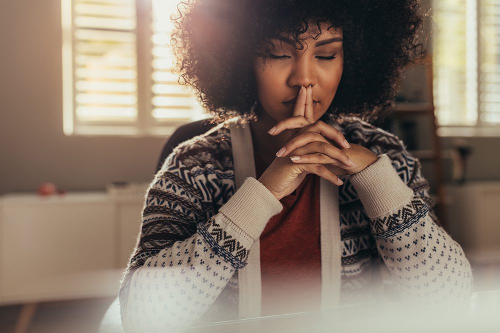 Woman sitting at her work desk and thinking with her eyes closed. Stressed woman taking a break to come up with solution using mindfulness.