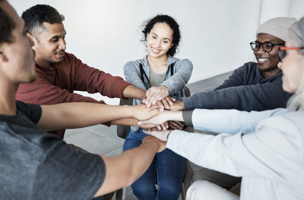 A circle of people with their hands in the middle.