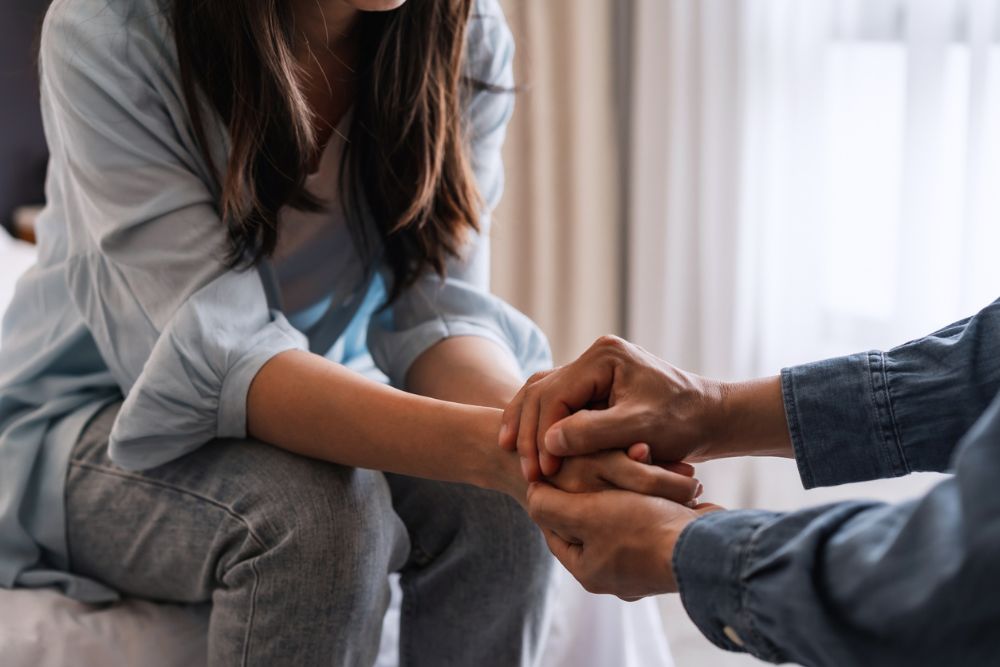 Close-up of two people holding hands in a supportive gesture, suggesting comfort, empathy, or emotional support during a difficult moment.
